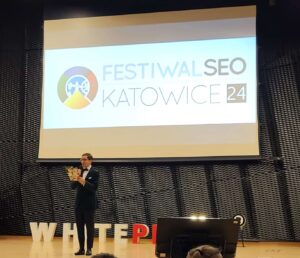 Festiwal SEO 2024 w Katowicach. Scena z wielkim ekranem, a na niej stoi konferansjer, Sławomir Borowski.